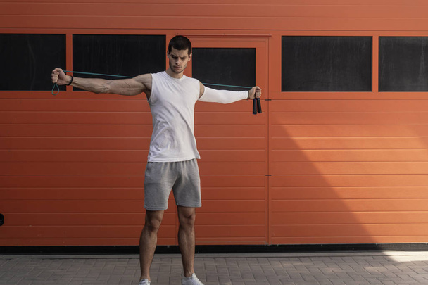 Porträt eines muskulösen jungen Mannes, der mit Springseil auf orangefarbenem Wandhintergrund trainiert - Foto, Bild