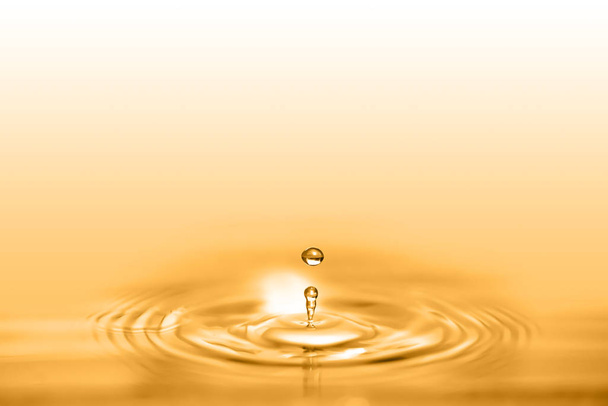 Zbliżenie na kroplę płynu kosmetycznych olej golden tworzenie okrągłą falą. - Zdjęcie, obraz