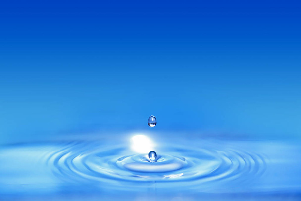 Крупный план по двойной капле воды, падающей в голубую жидкость и создающей круглую волну
. - Фото, изображение