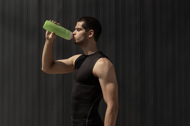 Sport model man drinkwater uit een plastic fles op grijze achtergrond met kopie ruimte. Portret gespierde man nemen van een pauze om te hydrateren zijn lichaam na een training. - Foto, afbeelding
