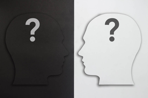 Two paper heads with a question mark, black and white on a black and white background. The concept of a split personality, different opinions, dispute, war. Flat lay, top view - Photo, Image