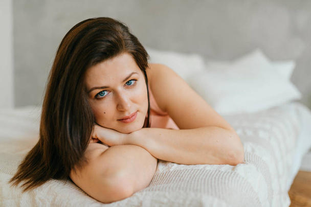 Beautiful brunette woman lying on white bed at home in morning - Foto, immagini