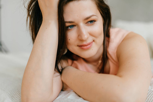 Beautiful brunette woman lying on white bed at home in morning - Foto, afbeelding