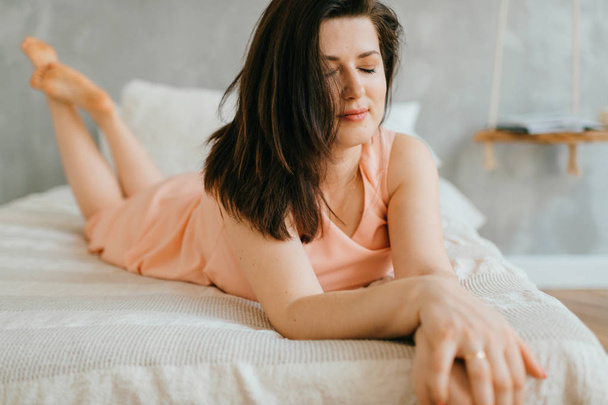 Beautiful brunette woman lying on white bed at home in morning - Φωτογραφία, εικόνα