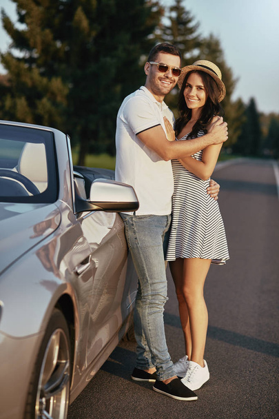 full length shot of smiling man leaning the cabrio, hugging his girlfriend and looking at the camera - 写真・画像