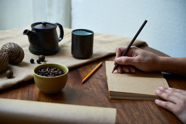 woman writing in opened notebook with pencil at wooden table - Photo, Image