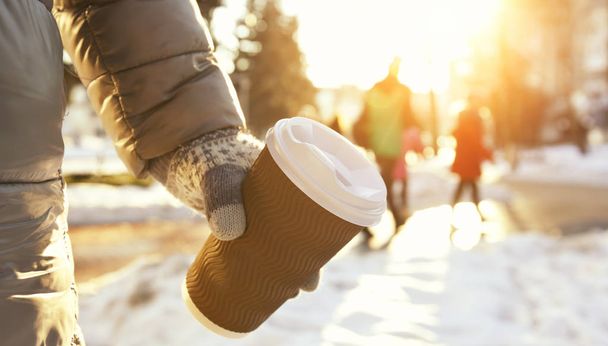 若い女性は冬の公園でコーヒーのテイクアウトのカップを保持します。 - 写真・画像