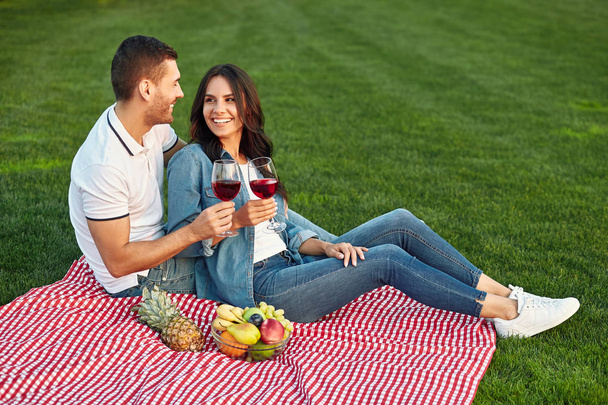 young couple having small picnic with fruits and wine in the park, looking at each other - Фото, зображення