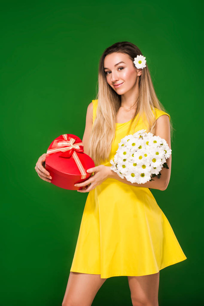 menina loira em um vestido amarelo detém um buquê de camomilas e uma caixa de presente
  - Foto, Imagem