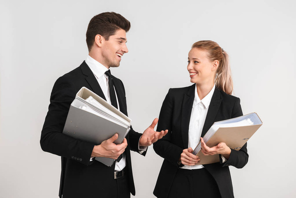 Cheerful young business couple standing isolated over gray background, holding folders with documents, talking - Фото, изображение