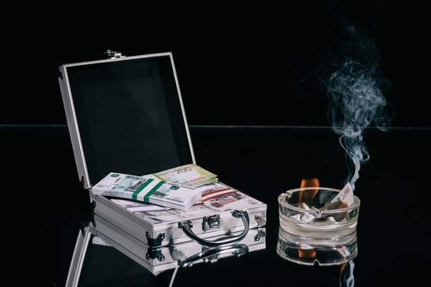 russian rubles banknotes in suitcase safe box and burning money in ashtray on black  - Photo, Image