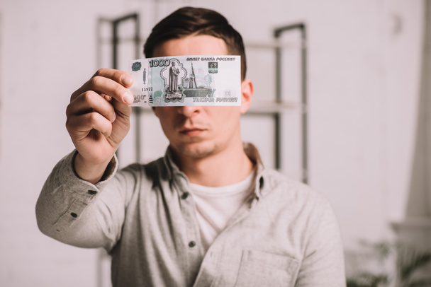νεαρός άνδρας που κρύβει το πρόσωπο πίσω από Ρωσικά ρούβλια τραπεζογραμματίων - Φωτογραφία, εικόνα