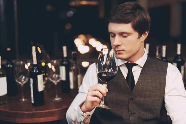 Confident handsome sommelier tasting wine in restaurant, holding glass in hand. - Photo, image