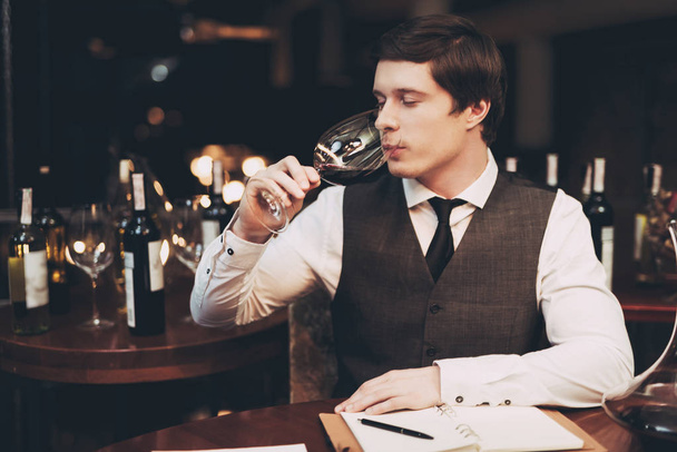 Young elegant sommelier studies aroma of wine in glass at restaurant. Wine tasting. - Foto, Bild