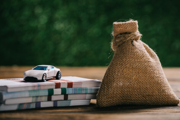 close-up view of sackcloth bag with money, rubles banknotes and model car on wooden table - Photo, Image