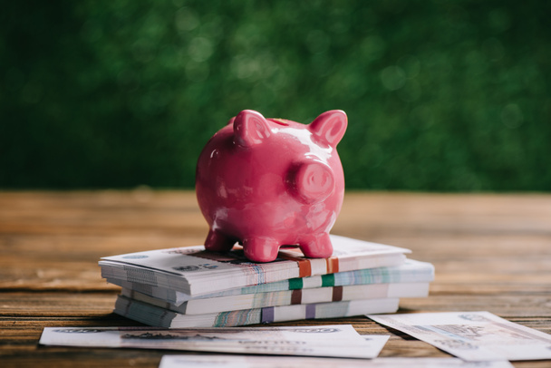 Nahaufnahme gestapelter Rubel-Banknoten und rosa Sparschwein auf Holztisch - Foto, Bild