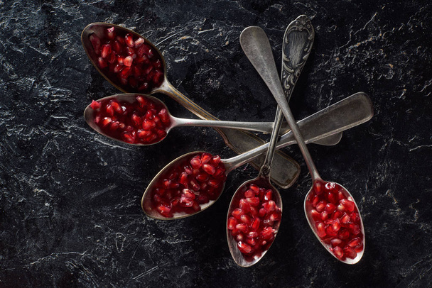 Flat lay of silverware and pomegranate seeds on dark background - Photo, Image
