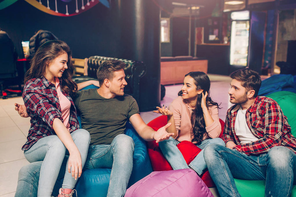 Four people sitting on inflatable bags in playing room and talk to each other. They smile and spend time together. People laugh. - Foto, immagini