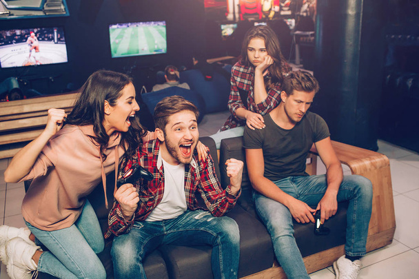Picture of happy couple cheering while second is upset. They win and lost game. Guys hold gamepads in hands. They sit together in playing room. - Fotoğraf, Görsel