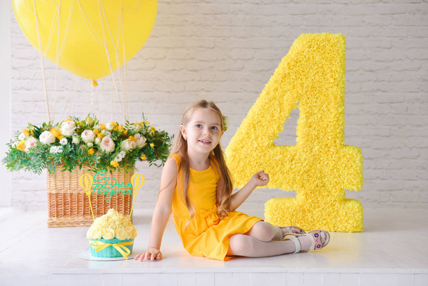 Birthday girl 4-5 years old is celebrating birthday in a decorated stylized studio, number 4 and big balloon. Yellow style. The inscription on the cake rerevod from Russian: Happy birthday - Foto, Imagen