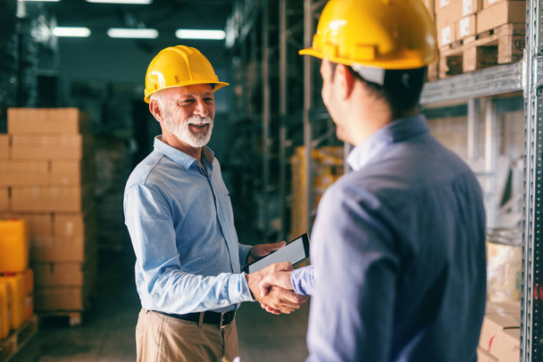 Deux hommes d'affaires serrant la main pour des affaires réussies tout en se tenant dans l'entrepôt
. - Photo, image