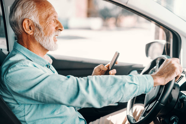 Közelkép a mosolygó szakállas vezető használ szúró telefon vagy üzenetet a autó vezetés közben. - Fotó, kép
