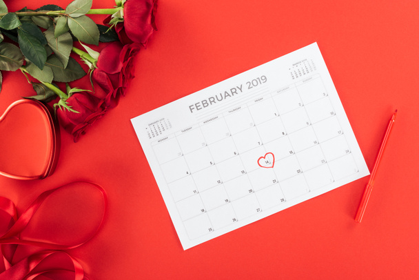 top view of roses and calendar with 14th february date marked with heart isolated on red, st valentines day concept - Photo, image
