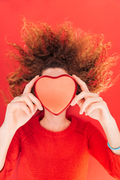 top view of girl holding heart symbol in front of face isolated on red, st valentines day concept - Photo, Image