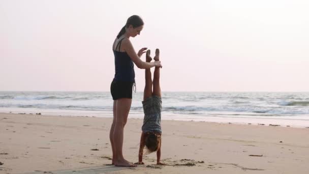 Sportieve jonge moeder met dochtertje gymnastische doen op het strand. - Video