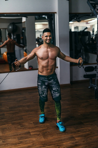 Strong shirtless bodybuilder doing exercises with exercise equipment. Gym interior. - Valokuva, kuva