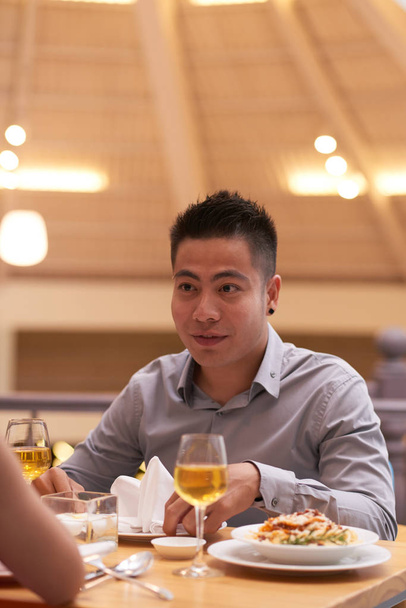 Jonge Aziatische man zitten aan de tafel en heeft een romantisch diner met zijn vriendin in het restaurant - Foto, afbeelding
