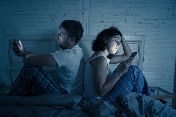 Young couple in bed late at night using smart phones obsessed with games, social media and apps ignoring each other in relationship communication problems and internet mobile addiction concept. - Fotó, kép