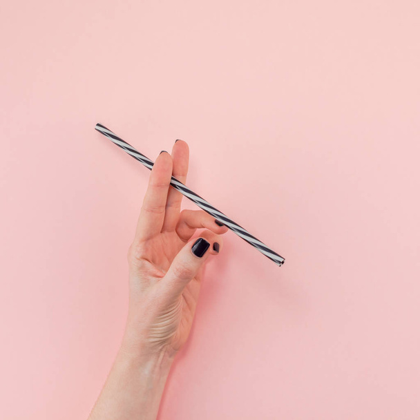 Creative top view flat lay of woman hand with black manicure holding cocktail drinking straw like cigarette with copy space pink paper background minimalism style. Template feminine blog social media - Foto, imagen