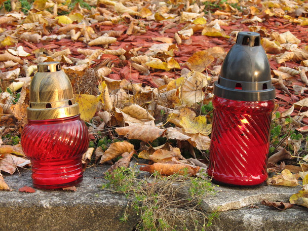dwa czerwone latarnie ze świecami na grobie pokryte opadłych liści jesienią - Zdjęcie, obraz