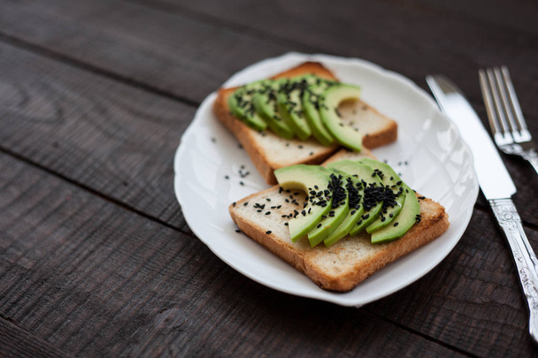 Výborný toast s avokádem plátky a černým sezamem. koncept zdravé snídaně. přípitek na bílé desce. dělat sendviče s avokádem na tmavé dřevěné pozadí. pohled shora zdravých biopotravin - Fotografie, Obrázek