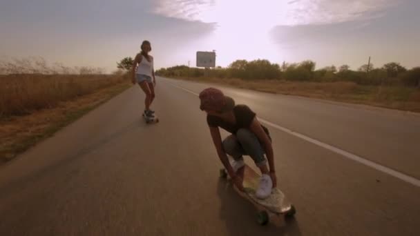 Two young fit women keeping balance while cruising on longboards during summer vacations in the countryside in Eastern Europe - Footage, Video