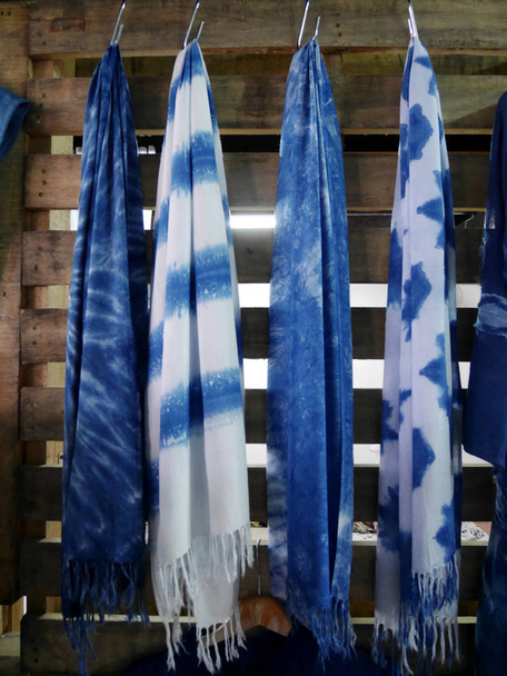 Scarf and shawl tie batik dyeing with mauhom indigo hanging on wooden wall in clothes shop for sale travelers people at market in Nonthaburi, Thailand - Photo, Image