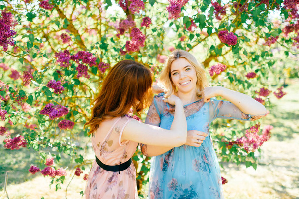 attractive twin sisters in different dresses in blooming summer botanical garden - Fotó, kép