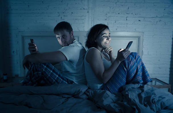 Lifestyle portrait of happy girlfriend wife addicted to mobile phone in bed and angry upset frustrated husband boyfriend bored on phone feeling ignored. Internet mobile addiction and Couple problems. - Foto, Bild