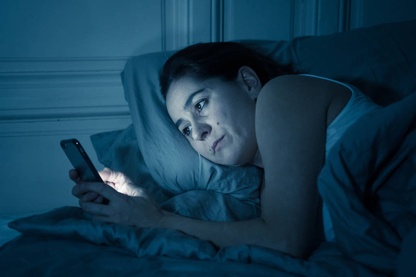 Зависимая молодая красивая женщина чата и серфинга в Интернете, используя свой смартфон сонный скучно и устал поздно ночью в Интернете, мобильная зависимость и бессонница концепции
. - Фото, изображение