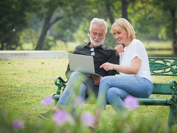 Two happy seniors retirement Man and woman are sitting and using computer laptop in park - Fotoğraf, Görsel