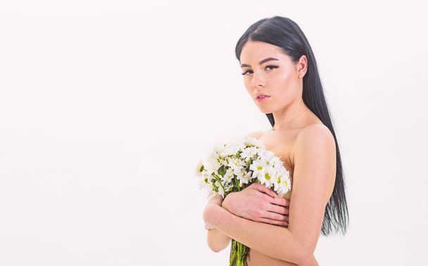 Lady covers breasts with flowers, isolated on white. Cancer of breast concept. Girl on calm face naked holds chamomile flowers in front of chest. Woman hiding her breasts, covers with bouquet - Photo, image