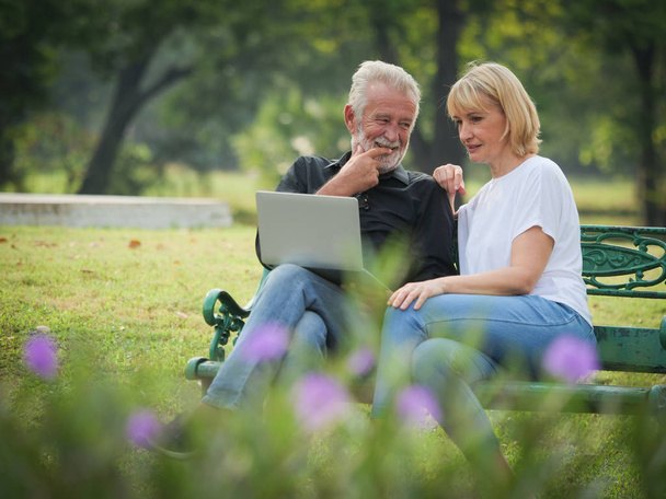 Two happy seniors retirement Man and woman are sitting and using computer laptop in park - Foto, imagen