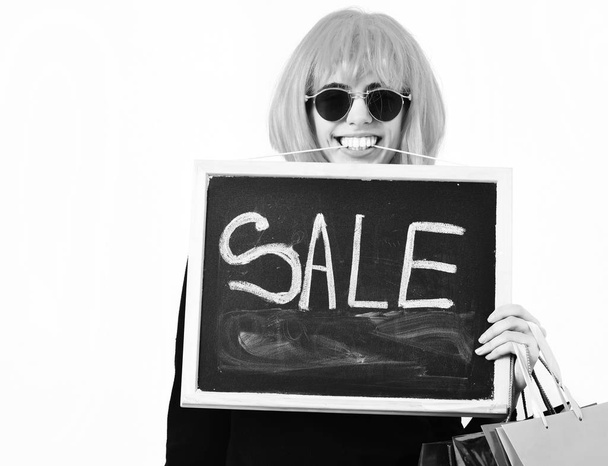 girl in wig holding package, hangers, board with sale inscription - Foto, afbeelding