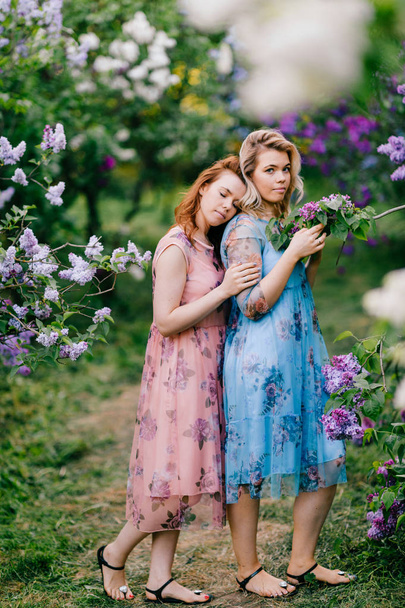  young tender twin sisters in blooming lilac botanical garden - Fotó, kép