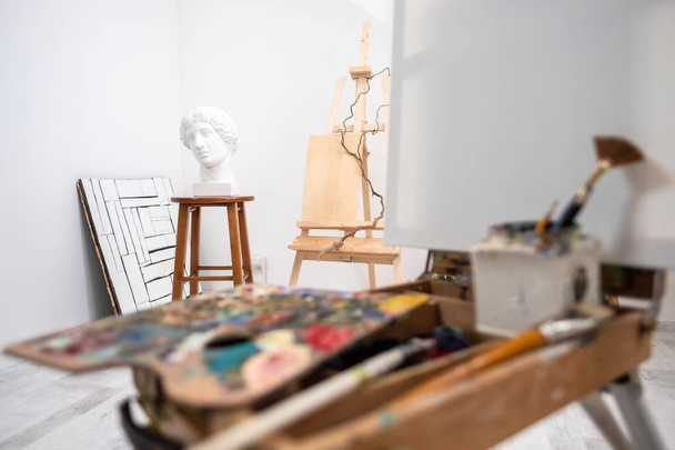 Interior of white studio of the artist, creative person. Easel, brushes, plaster head and figures. Attic, high ceilings. - 写真・画像