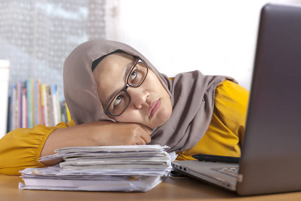 Retrato de asiático muçulmano empresária olhando cansado sonolento e preguiçoso esperando por má conexão à internet na frente de seu laptop no escritório
 - Foto, Imagem
