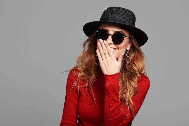 Retrato de moda mujer bonita en el sombrero de estilo rock negro y gafas de sol sobre fondo gris tienen una diversión y sonrisa. Concepto de vacaciones
 - Foto, Imagen