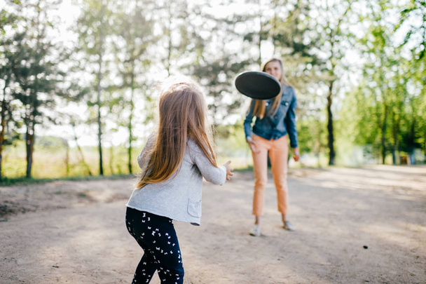 joven madre e hija pequeña jugando con disco volador en el parque
 - Foto, Imagen