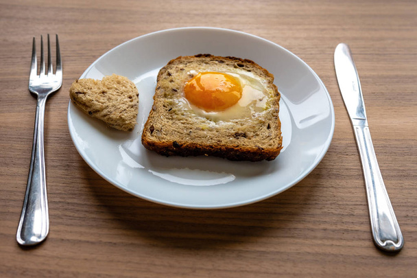 Breakfast concept. White plate with hearts of bread, baked bread and egg. Wooden texture background. - Фото, зображення